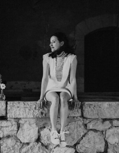 Photo de la robe Edwige en noir et blanc, portée par une femme assise sur un mur en pierre