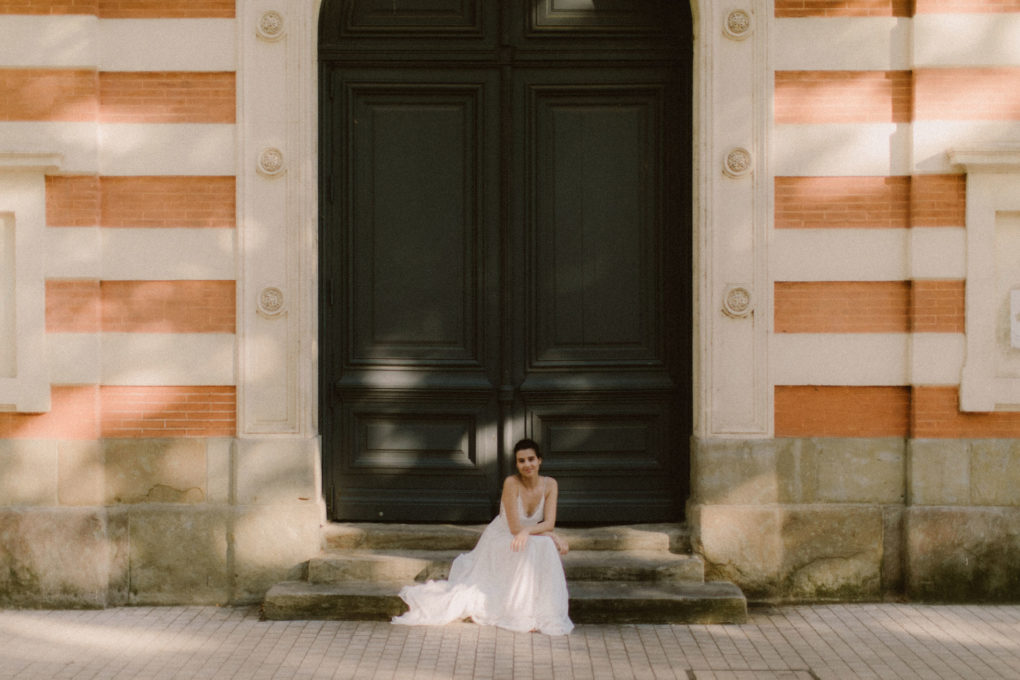 Plan d'ensemble de la robe Laura portée par une femme assise sur des marches devant une porte d'entrée